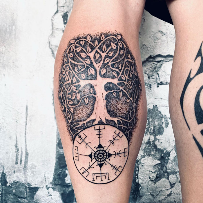 Unique calf tattoo featuring a detailed tree and compass design on a textured background.