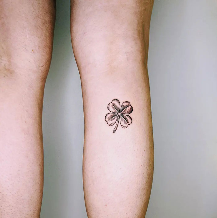 Four-leaf clover tattoo on calf, showcasing minimalist design and symbolizing luck and coolness.