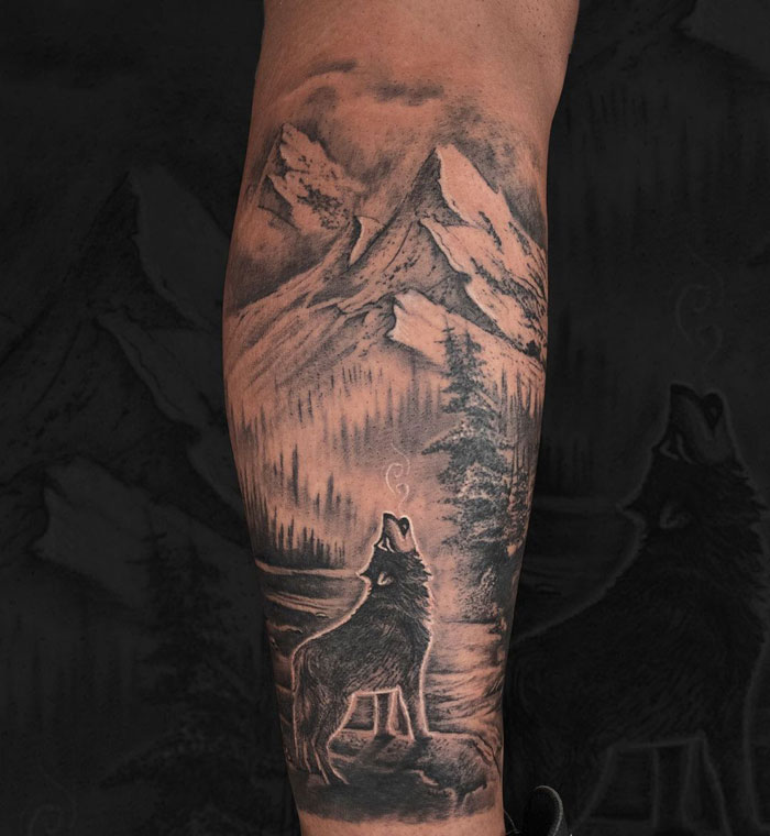 Wolf howling with mountain scenery calf tattoo, showcasing pure coolness.