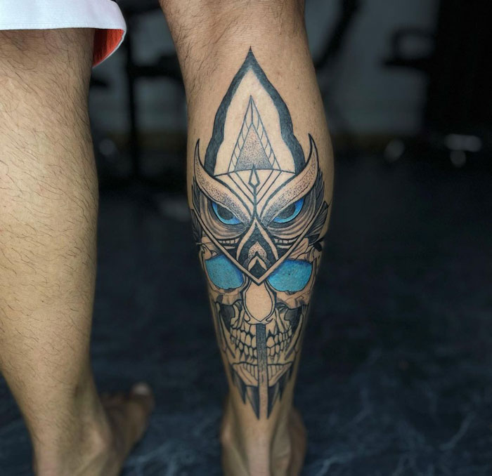Stylized owl tattoo design on a lower leg showcasing intricate details and bold colors.