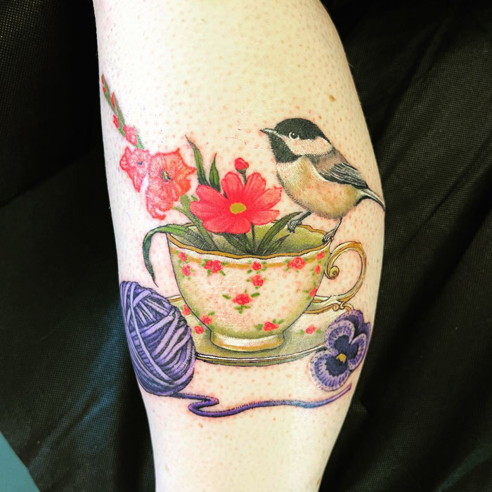 Calf tattoo featuring a bird, flowers in a teacup, and a ball of yarn for cool ink inspiration.
