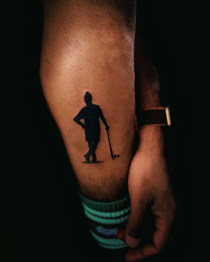 Silhouette tattoo on a lower leg featuring a golfer with a club.