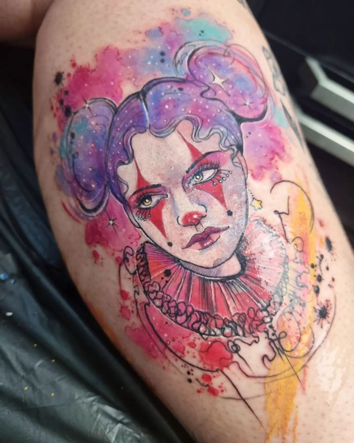 Colorful clown portrait calf tattoo with abstract watercolor splashes.