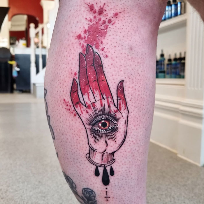 Unique calf tattoo featuring a detailed hand with an eye design, accented with red and black ink.