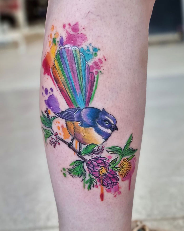 Colorful bird and floral design on calf tattoo, showcasing unique calf tattoo ideas with vibrant rainbow tail and blossoms.
