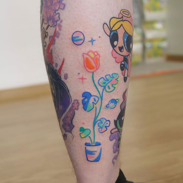 Colorful lower leg tattoo featuring a cartoon character, vibrant flowers, and abstract elements.