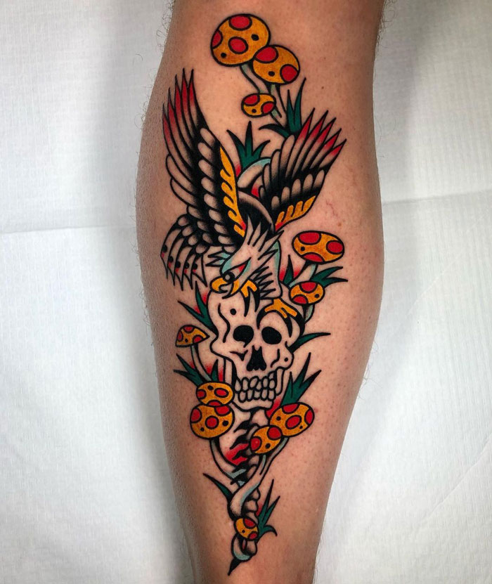Colorful lower leg tattoo featuring a skull, eagle, and mushrooms.