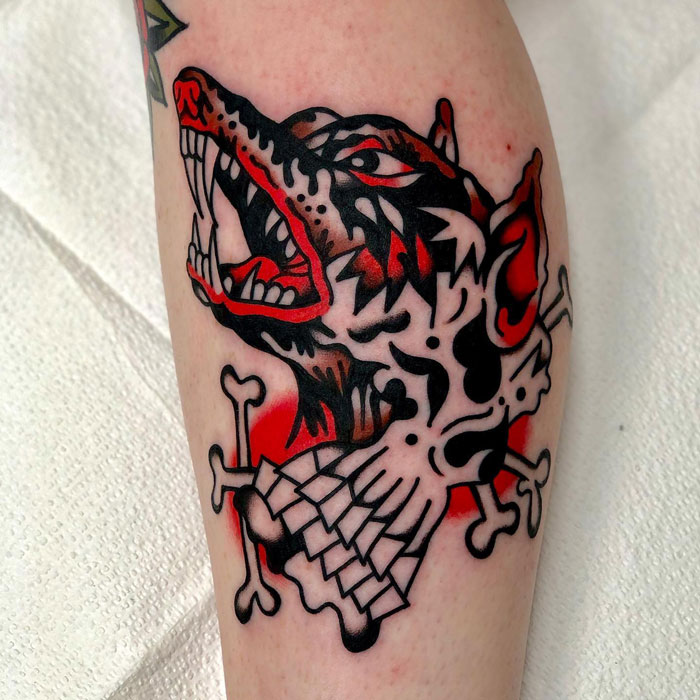 Bold lower leg tattoo featuring an aggressive wolf with geometric patterns and vibrant red accents.
