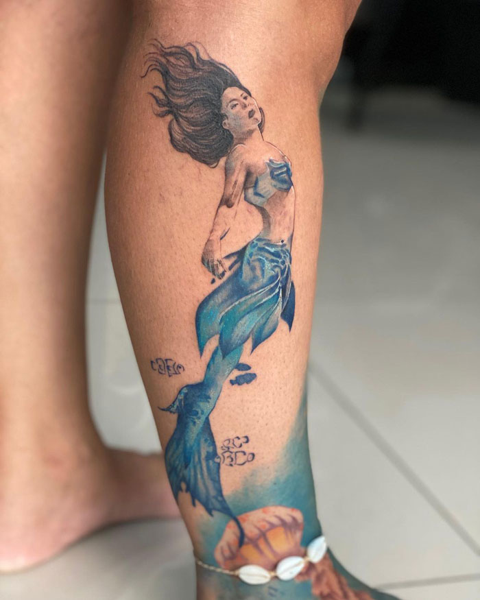 Mermaid lower leg tattoo with blue hues and flowing hair, showcasing intricate design and artistry.