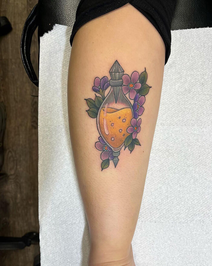 Colorful calf tattoo of a potion bottle surrounded by lavender flowers and green leaves.