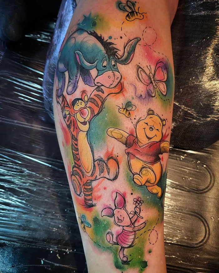 Colorful calf tattoo featuring Eeyore, Tigger, Pooh, and Piglet with butterflies, showcasing unique design ideas.