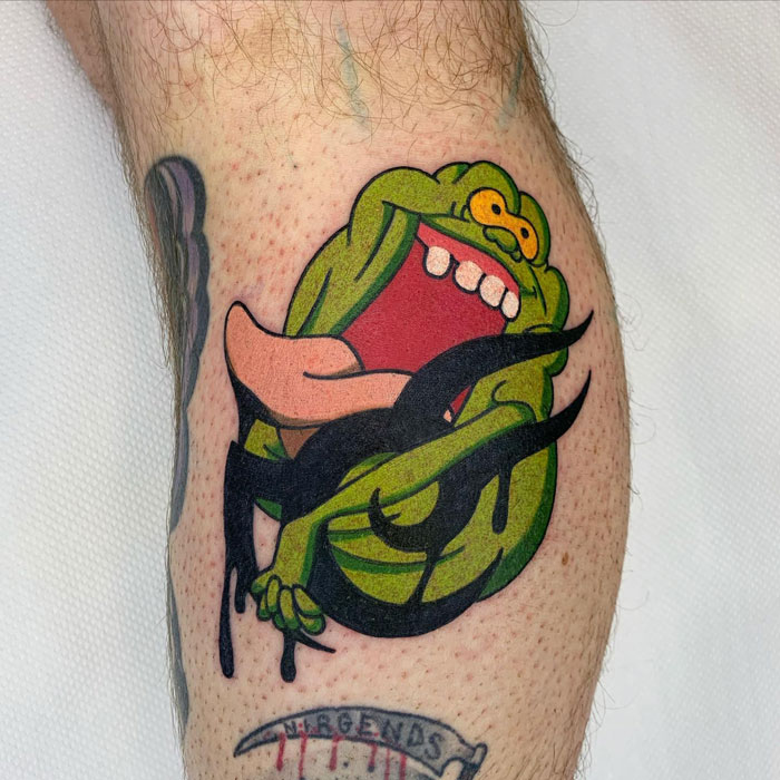 Unique calf tattoo featuring a green cartoon character with a wide-open mouth and tattoo lettering below.