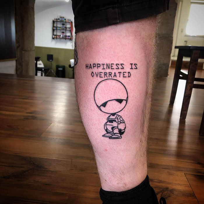 Cool calf tattoo featuring a minimalist design with text "Happiness is Overrated" above a cartoon character.