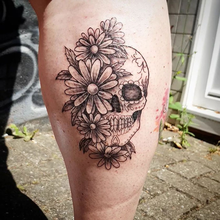 Lower leg tattoo featuring a skull adorned with flowers, showcasing detailed artistry in black ink.
