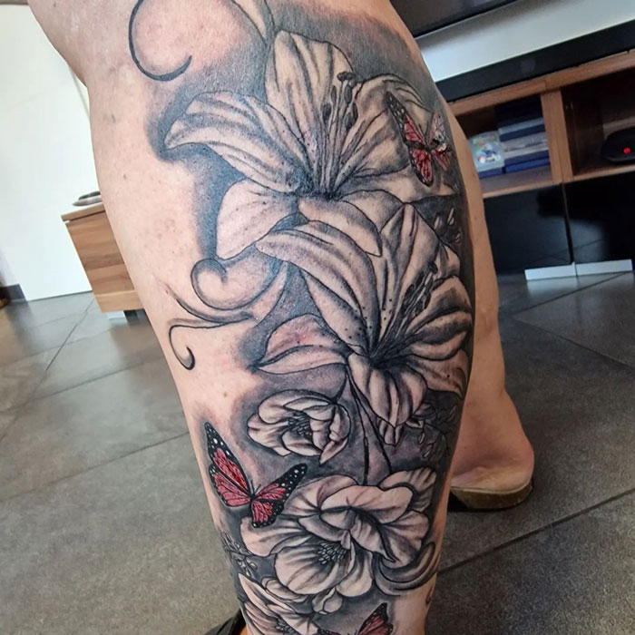 Floral calf tattoo featuring lilies and red butterflies, showcasing cool tattoo design ideas.