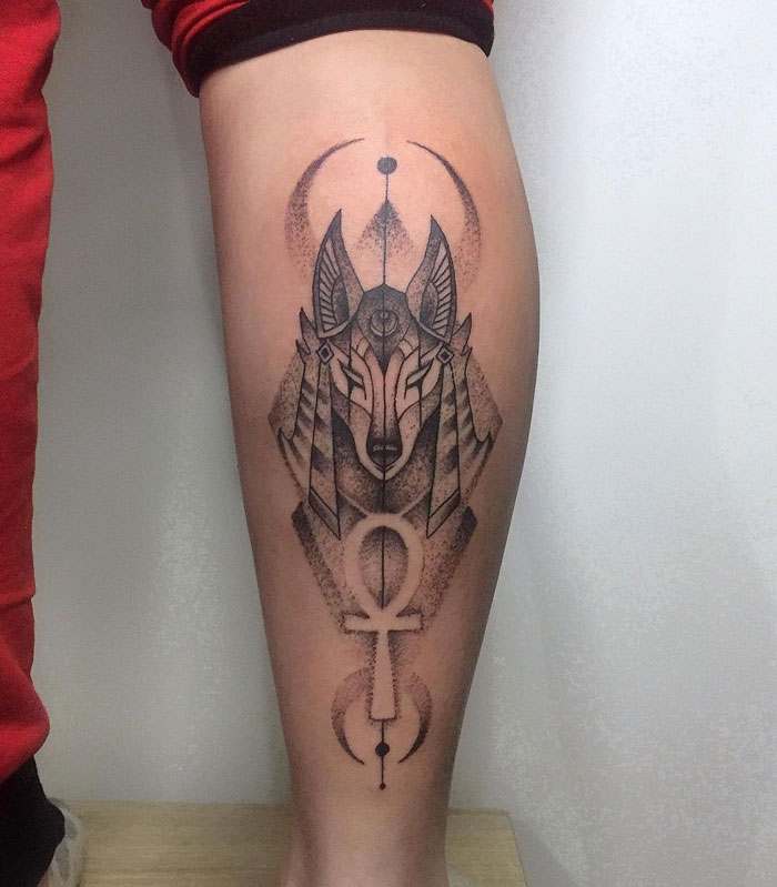Geometric calf tattoo featuring a stylized Anubis symbol with intricate dotwork design.