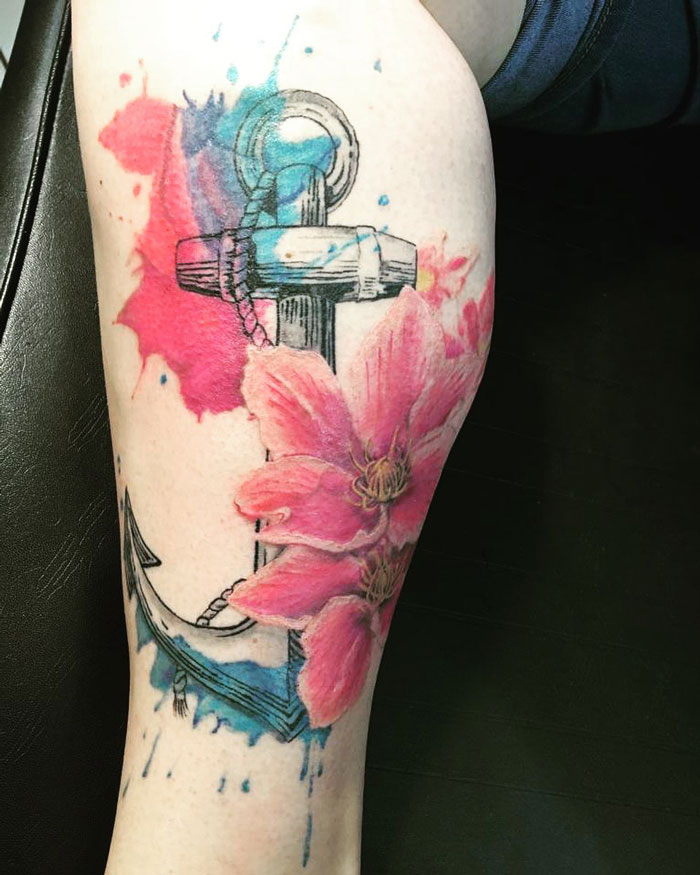 Watercolor anchor calf tattoo with pink flowers and blue splashes, showcasing unique tattoo coolness.