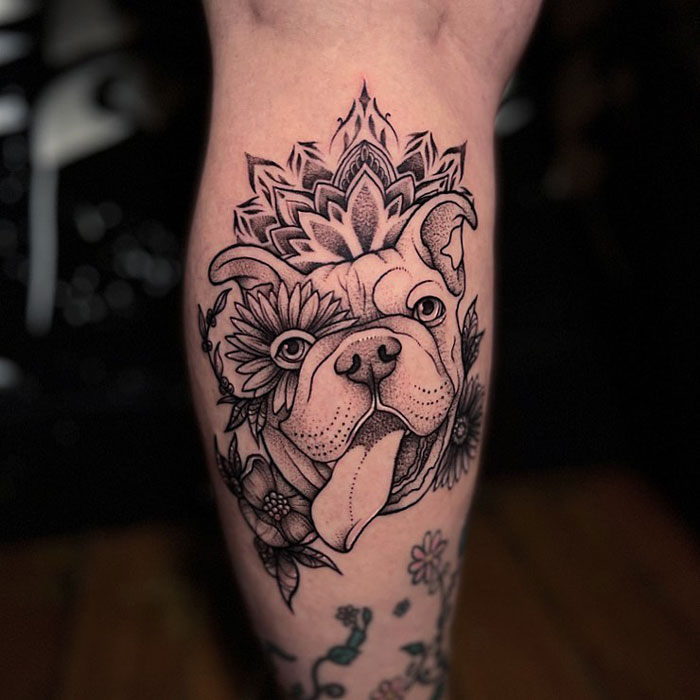 Lower leg tattoo of a dog with floral designs and a mandala on the calf.
