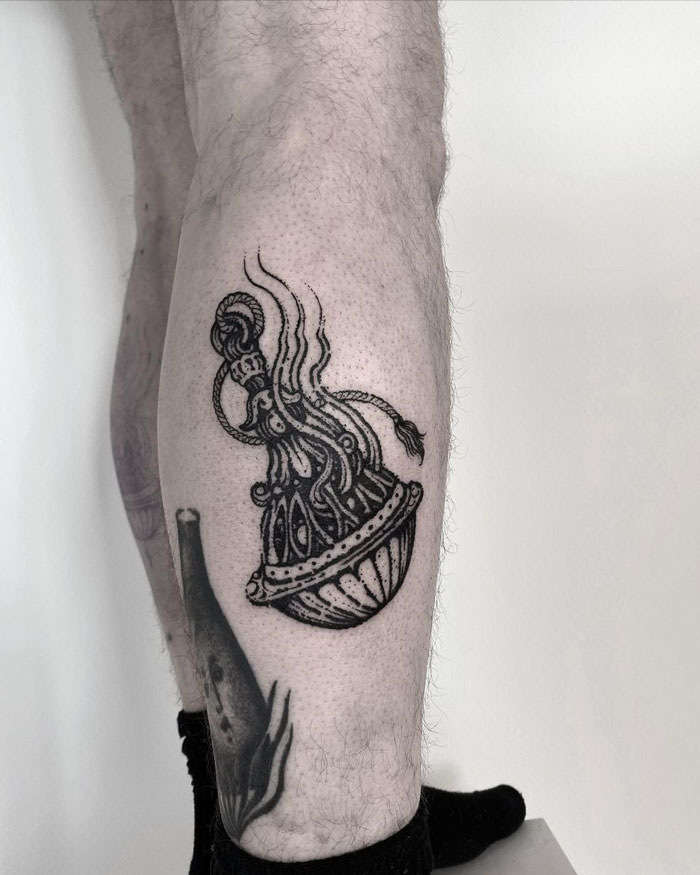 Ornate black calf tattoo featuring a detailed vase design against a neutral background.