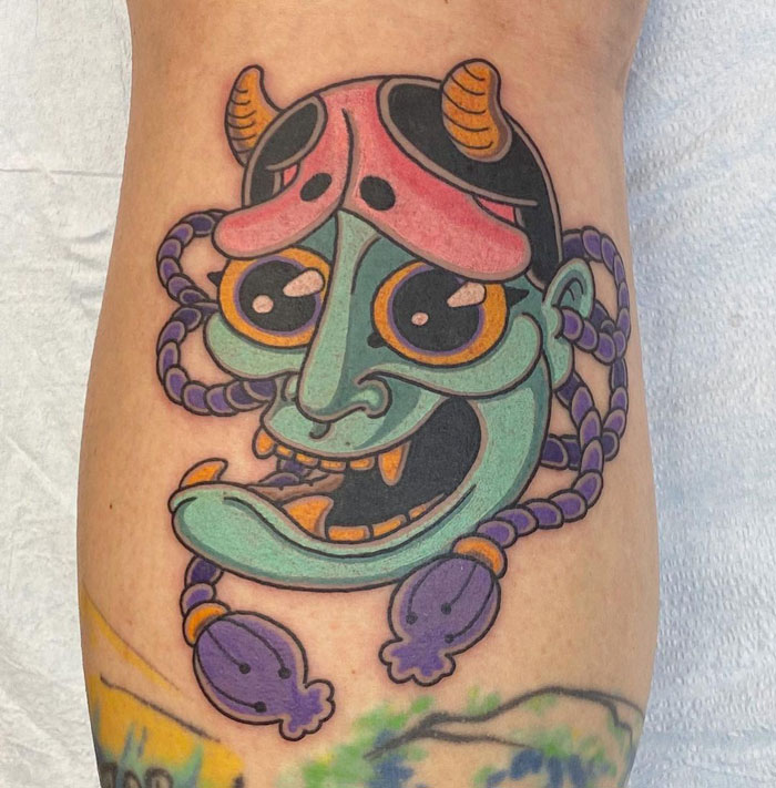 Colorful mask-inspired lower leg tattoo featuring vibrant hues.