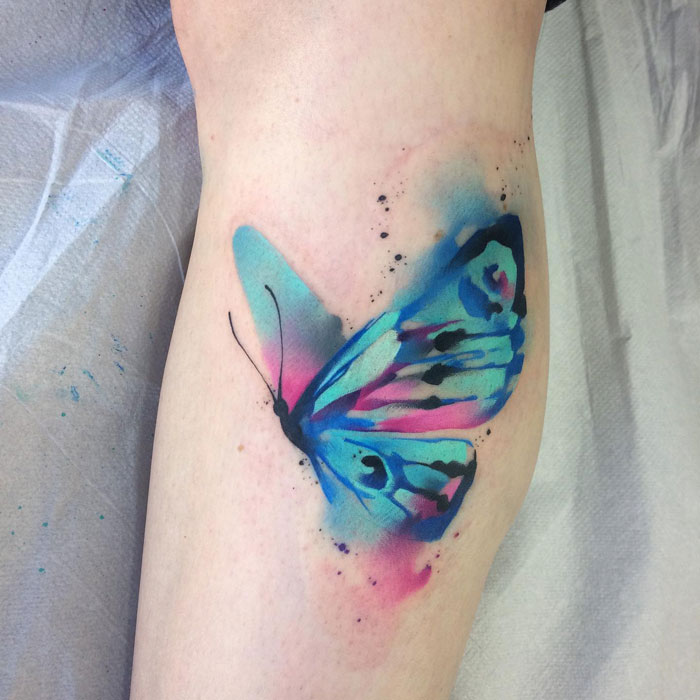 Colorful butterfly lower leg tattoo featuring blue and pink hues.
