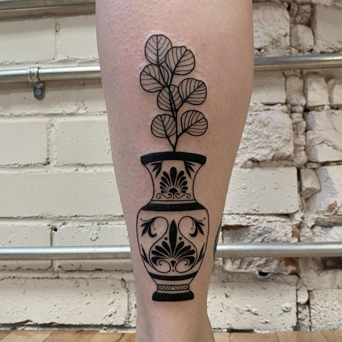 Calf tattoo with a detailed decorative vase and leafy plant design.