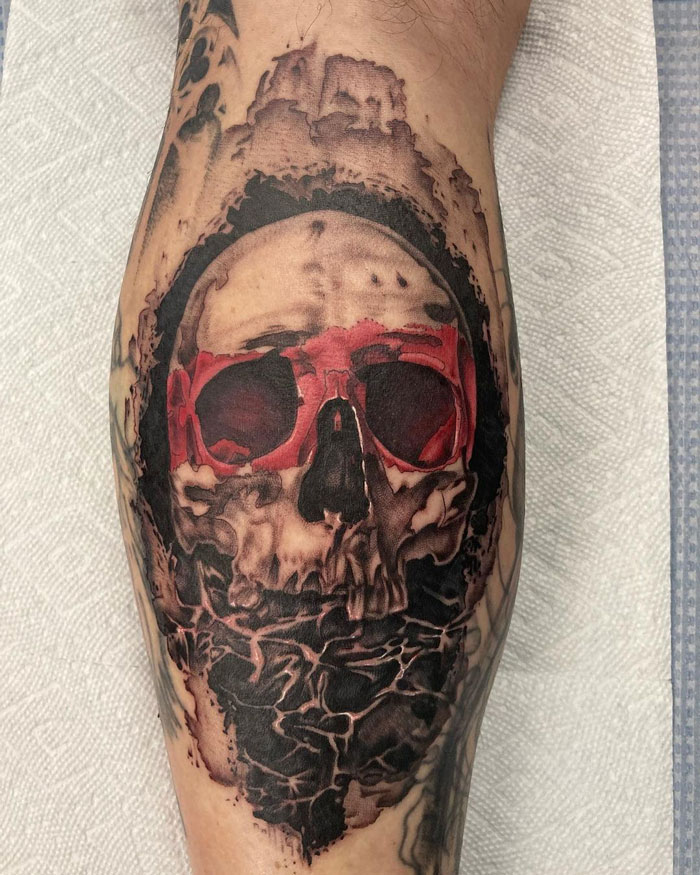 Unique calf tattoo featuring a skull wearing red sunglasses in a bold, artistic style.