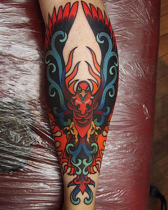 Colorful phoenix design on calf tattoo, showcasing vibrant reds and blues in a unique pattern.