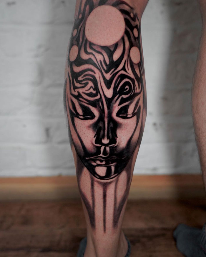 Unique abstract face tattoo design on calf, featuring bold black and white lines and circular patterns.