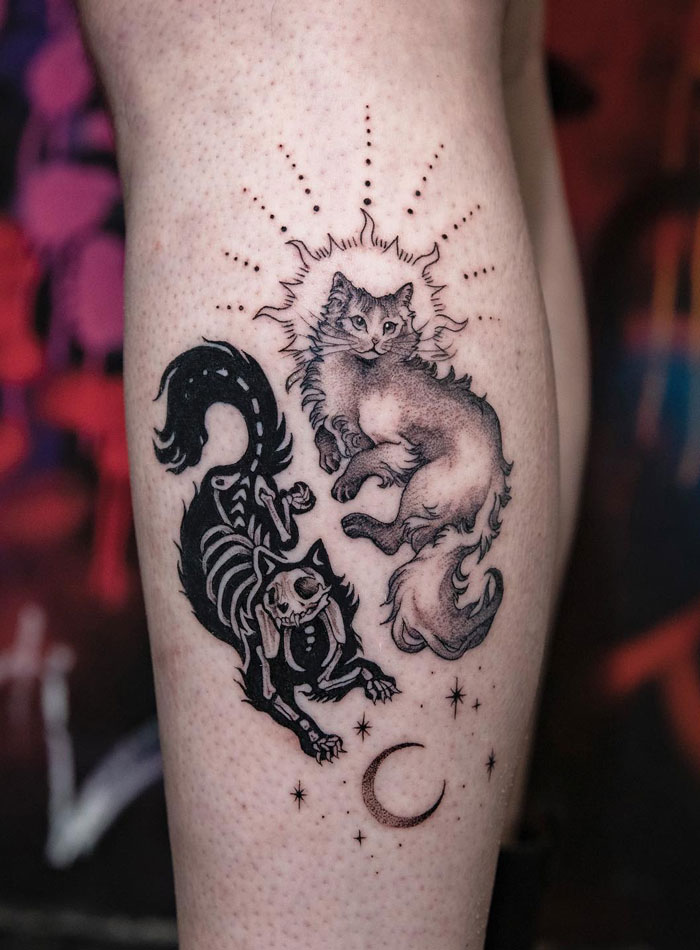 Lower leg tattoo featuring two cats, one celestial and one skeletal, surrounded by stars and a crescent moon.