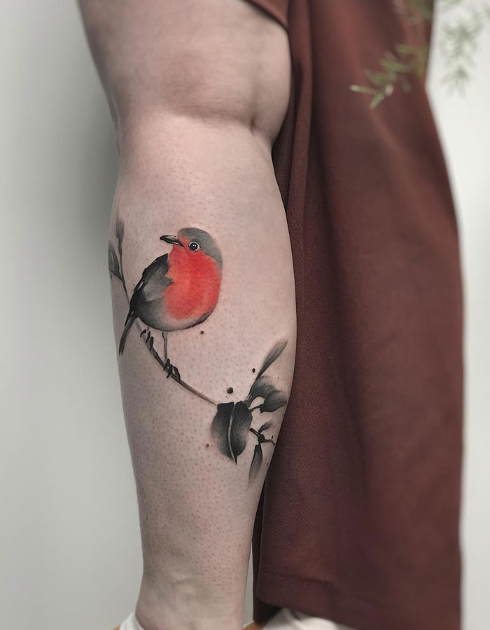 Calf tattoo featuring a colorful bird perched on a branch, showcasing unique design elements.