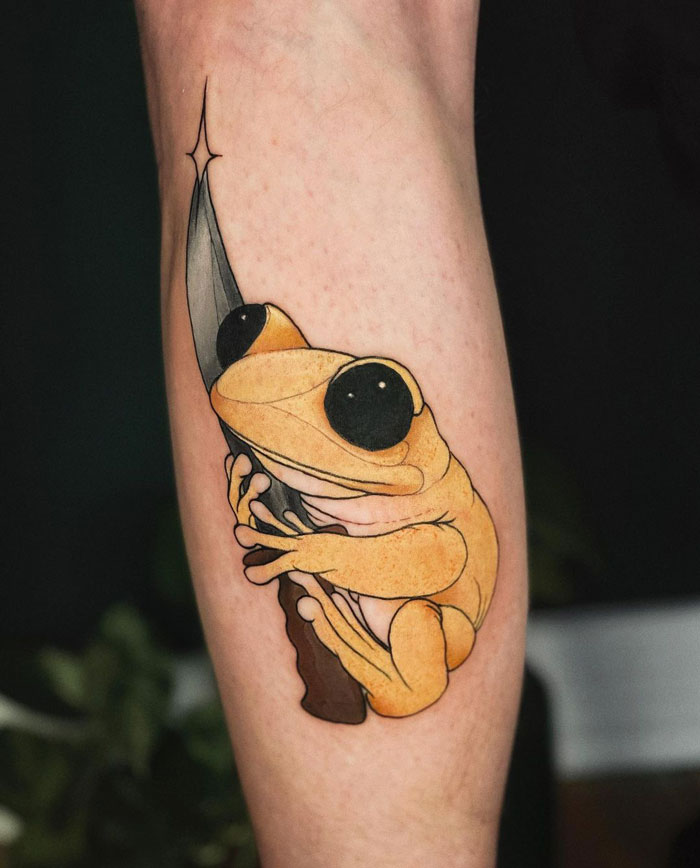 Yellow frog tattoo on calf, clinging to a knife, showcasing coolness and artistic flair.