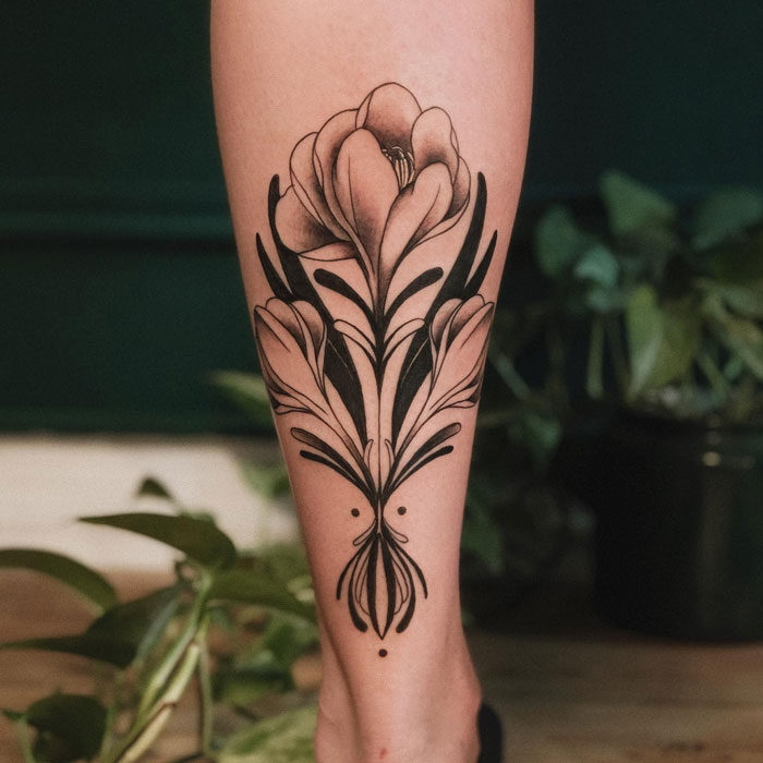Floral lower leg tattoo design with black ink showcasing detailed petals and leaves.