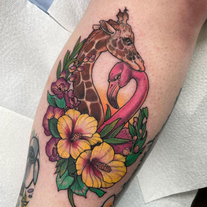 Unique calf tattoo featuring a giraffe, flamingo, and vibrant flowers, showcasing colorful and artistic design.