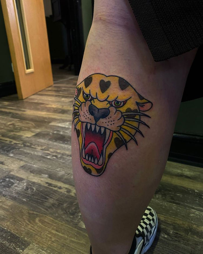Lower leg tattoo of a colorful snarling leopard head on a person's calf.