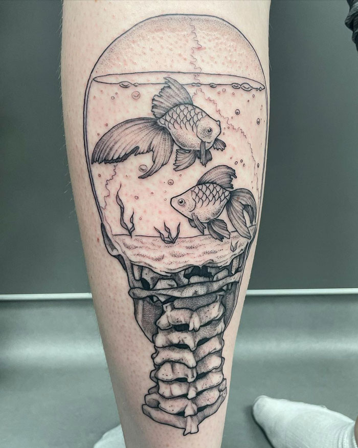 Lower leg tattoo featuring two fish in an aquarium design with skeletal elements.