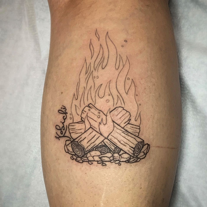 Lower leg tattoo of a campfire with logs and flames on skin.