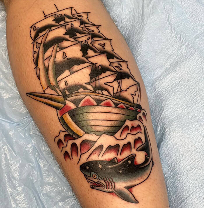 Intricate calf tattoo featuring a ship riding waves above a menacing shark, highlighting cool tattoo artistry.
