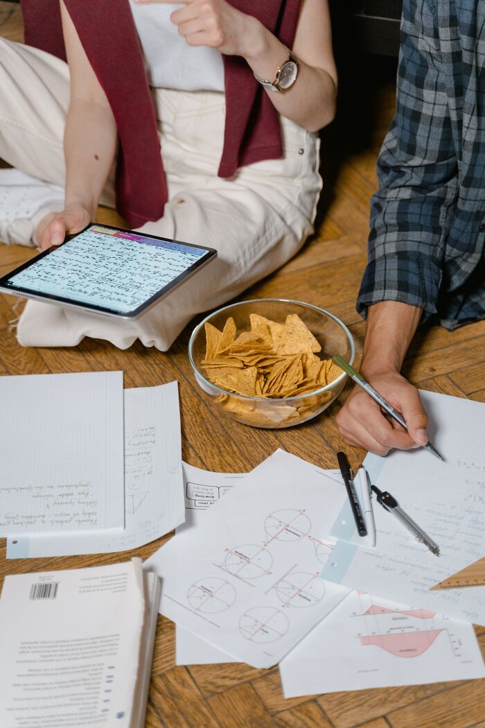 Two people studying geometry with papers, tablet, and snacks, illustrating entertaining it doesn't work like that stories.