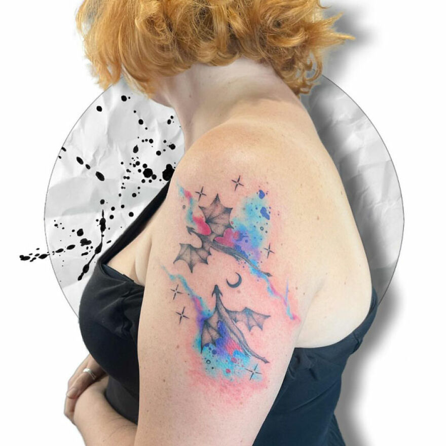 Colorful watercolor tattoo featuring abstract wings and stars on a woman's upper arm.
