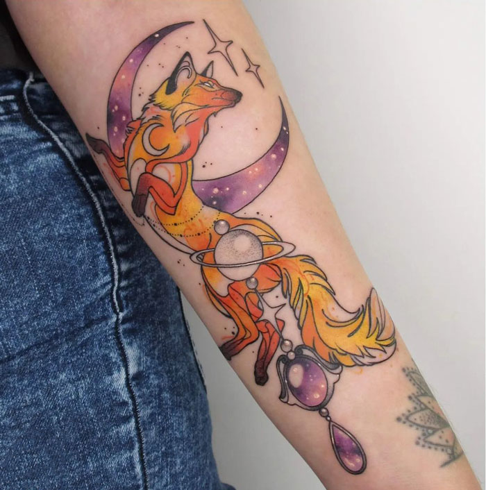 Colorful fox and cosmic elements watercolor tattoo on forearm, showcasing ethereal design.