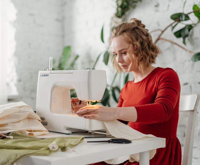A woman sewing at home, focusing intently on fabric under a sewing machine.