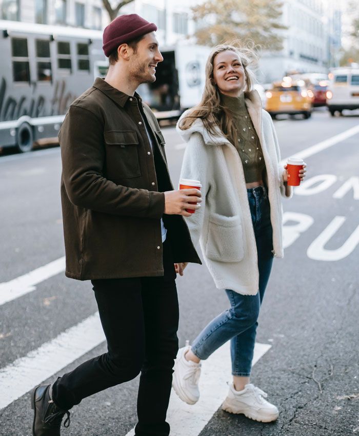 Couple walking outdoors with coffee, smiling and enjoying each other's company.