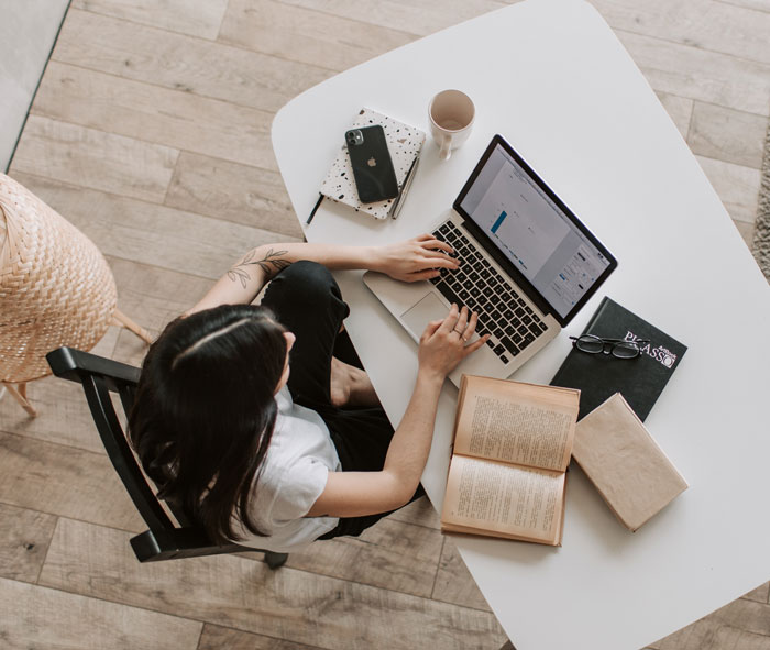 Person working on a laptop at home, surrounded by books and coffee, finding fun things to avoid boredom.