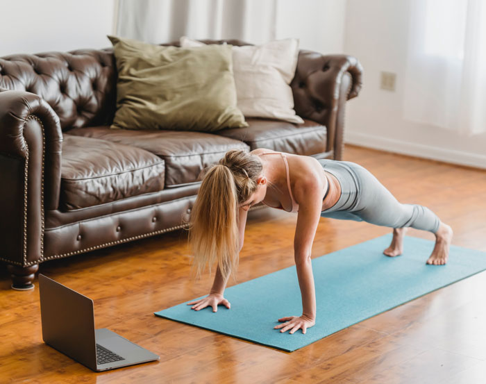 Woman doing yoga at home on a mat in front of a laptop, exercising to avoid boredom.