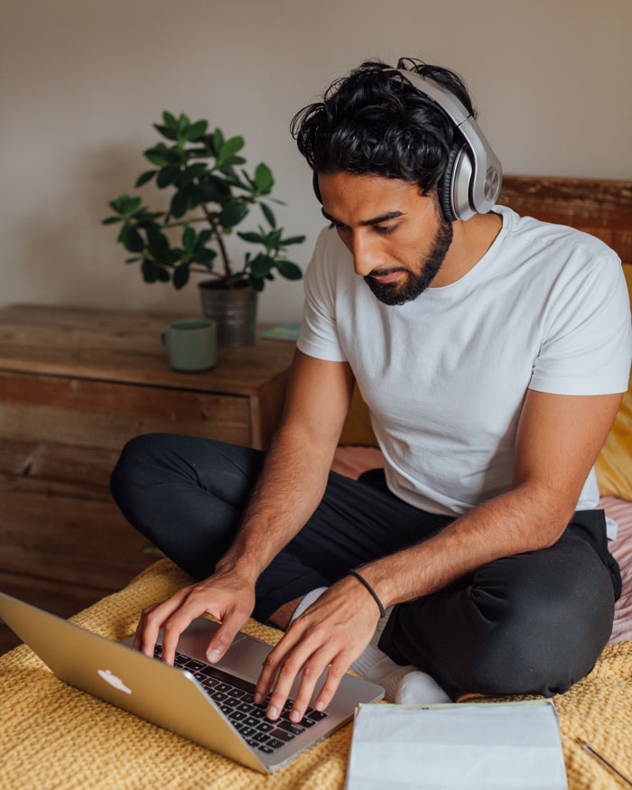 Person wearing headphones, typing on a laptop at home, avoiding boredom with indoor activities.