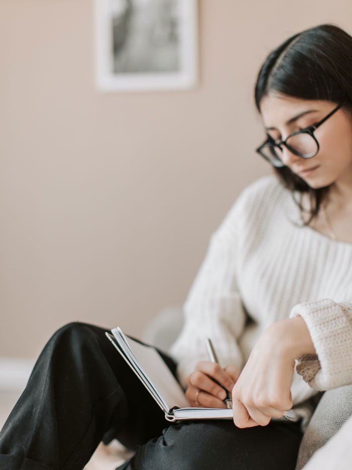 A woman in glasses writing in a notebook at home, finding fun ways to avoid boredom.