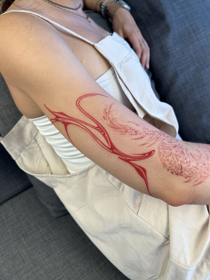 A red flowing tattoo design inspired by traditional marbling on a person's arm, wearing a white top. A red flowing tattoo design inspired by traditional marbling on a person's arm, wearing a white top.
