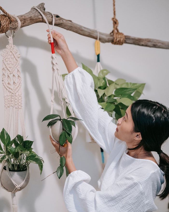 Woman engaging in fun home activity by arranging plants in macrame hangers.