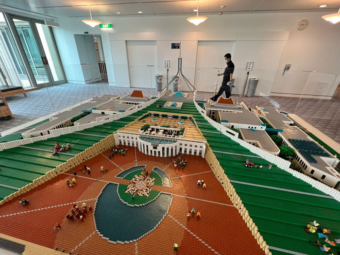 Detailed LEGO builds showcasing an intricate architectural model with miniature figures and green landscaping in an indoor setting.